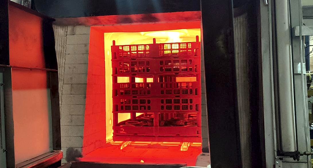 Sealed quench furnace chamber glowing at temperature, door open, with a loaded fixture basket inside